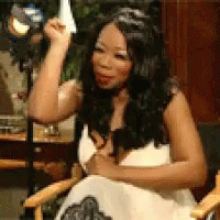 A Woman In A White Dress Is Sitting In A Chair With Her Arm Raised GIF
