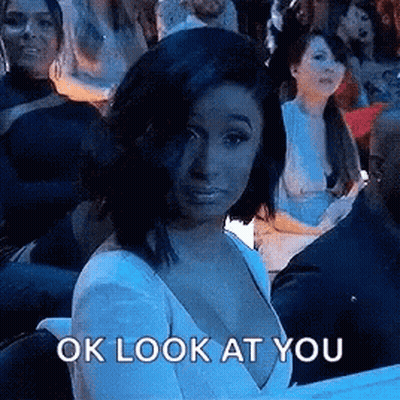 A Woman In A White Dress Is Sitting In A Crowd Of People And Looking At The Camera . GIF
