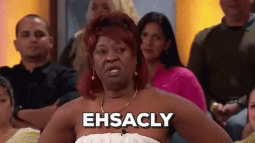 A Woman In A White Dress Is Sitting In A Crowd Of People And Saying Ehsacly . GIF