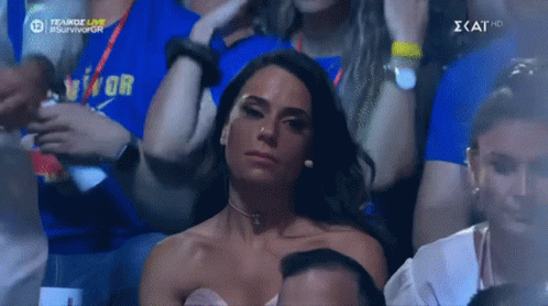A Woman In A White Dress Is Sitting In A Crowd Of People With A Blue Shirt That Says Vitor On It GIF