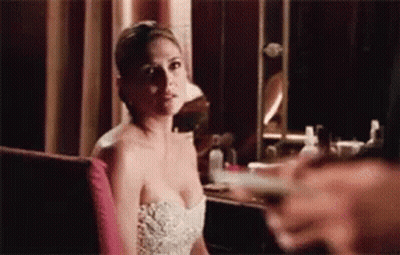 A Woman In A White Dress Is Sitting In Front Of A Mirror Looking At The Camera . GIF