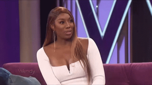 A Woman In A White Dress Is Sitting On A Purple Couch And Talking To Someone . GIF