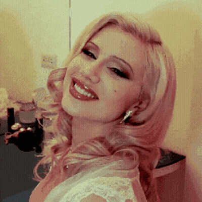 A Woman In A White Dress Is Smiling And Looking At The Camera GIF