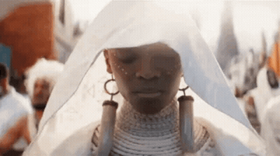 A Woman In A White Dress Is Standing In A Crowd Of People . GIF