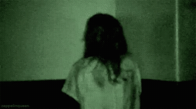 A Woman In A White Dress Is Standing In A Dark Room With A Green Light Behind Her . GIF