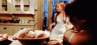 A Woman In A White Dress Is Standing In A Kitchen With A Bowl Of Bread On The Table . GIF