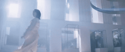 A Woman In A White Dress Is Standing In A Room With A Lot Of Windows . GIF
