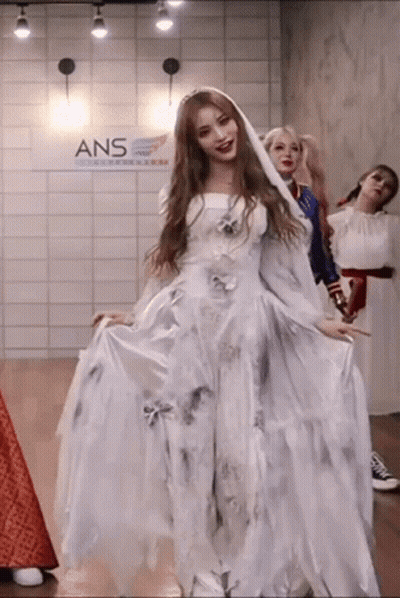 A Woman In A White Dress Is Standing In A Room With Other Women Dressed In Costumes . GIF