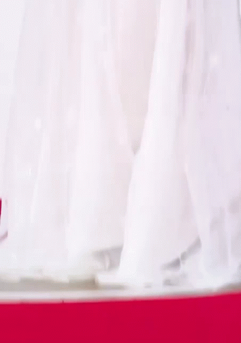 A Woman In A White Dress Is Standing In Front Of A Blue Wall . GIF