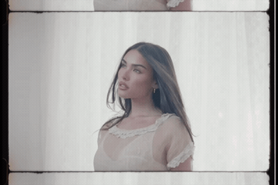 A Woman In A White Dress Is Standing In Front Of A White Curtain GIF