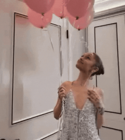 A Woman In A White Dress Is Standing In Front Of A White Wall GIF