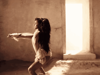 A Woman In A White Dress Is Standing In Front Of A Window GIF