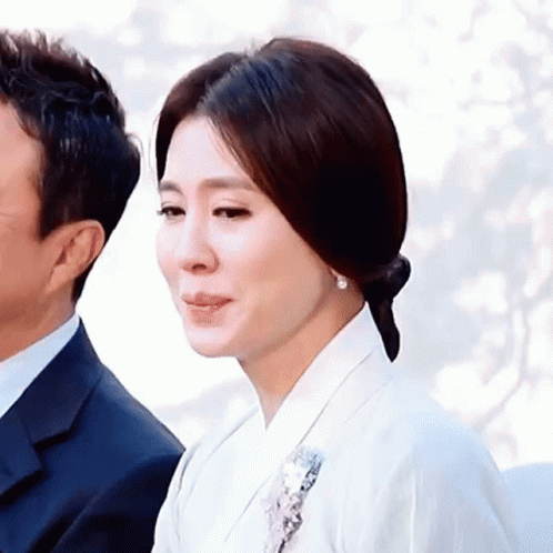 A Woman In A White Dress Is Standing Next To A Man In A Suit . GIF