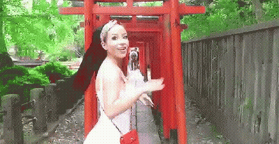 A Woman In A White Dress Is Standing Next To A Red Torii Gate . GIF
