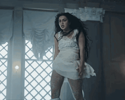 A Woman In A White Dress Is Standing Next To A Window GIF
