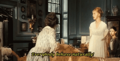 A Woman In A White Dress Is Standing Next To Another Woman In A Living Room And Saying Everybody Behave Naturally . GIF