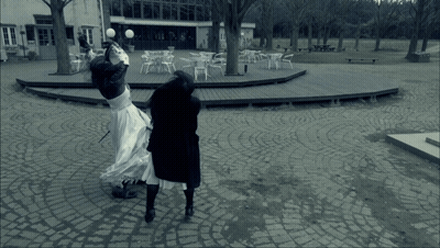 A Woman In A White Dress Is Standing On A Cobblestone Walkway GIF