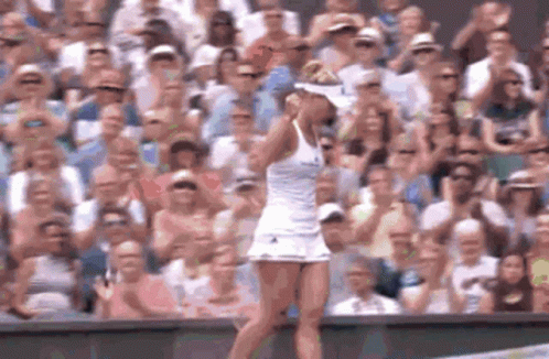 A Woman In A White Dress Is Standing On A Tennis Court In Front Of A Crowd Of People GIF