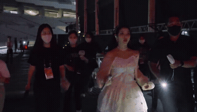 A Woman In A White Dress Is Surrounded By People Wearing Masks And A Man Holding A Flashlight .. GIF