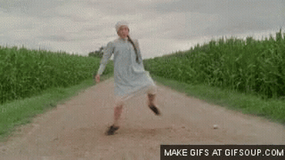 A Woman In A White Dress Is Walking Down A Dirt Road In A Field . GIF