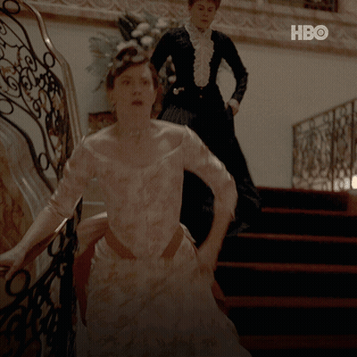 A Woman In A White Dress Is Walking Down A Set Of Stairs Next To A Woman In A Black Dress GIF