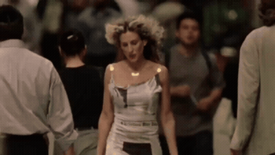 A Woman In A White Dress Is Walking In A Crowd Of People . GIF