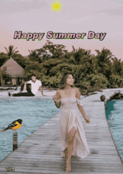 A Woman In A White Dress Is Walking On A Dock With A Man Sitting On The Beach Behind Her And The Words Happy Summer Day GIF
