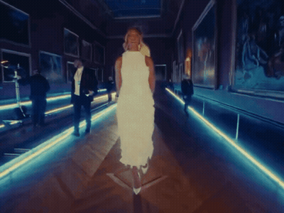 A Woman In A White Dress Is Walking Through A Dark Hallway GIF