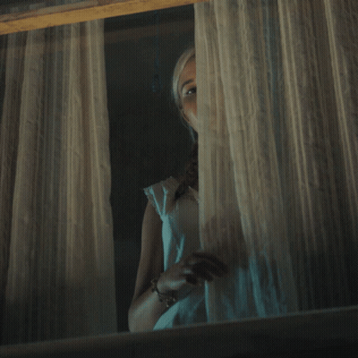 A Woman In A White Dress Looks Out A Window At Night GIF