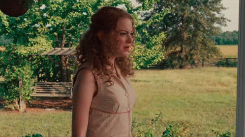 A Woman In A White Dress Stands In A Grassy Field GIF