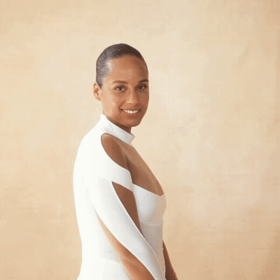 A Woman In A White Dress Stands In Front Of A Beige Background GIF