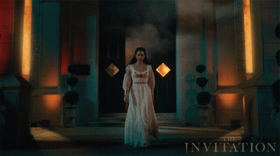 A Woman In A White Dress Stands In Front Of A Building With The Invitation Written On It GIF