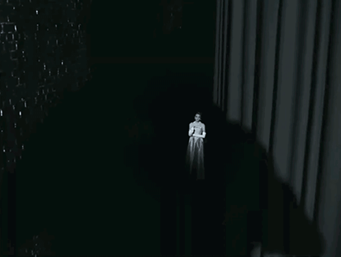 A Woman In A White Dress Stands In The Dark GIF