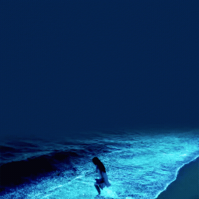 A Woman In A White Dress Stands In The Ocean GIF