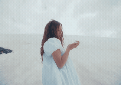 A Woman In A White Dress Stands On A Beach GIF