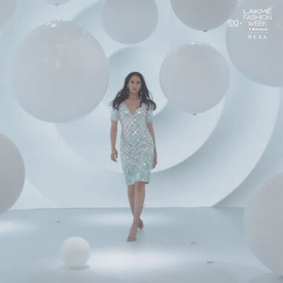 A Woman In A White Dress Walks Down A Runway At Lakme Fashion Week GIF