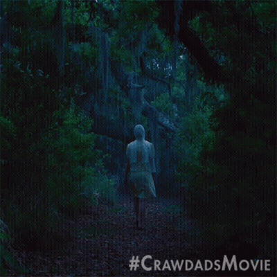 A Woman In A White Dress Walks Through A Dark Forest GIF