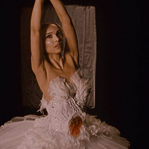 A Woman In A White Dress With Feathers On It Holds Her Arms Up GIF