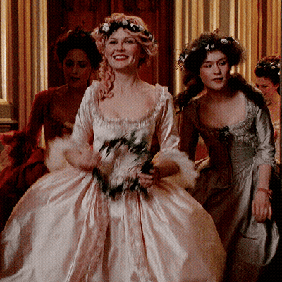 A Woman In A White Dress With Flowers In Her Hair Smiles GIF