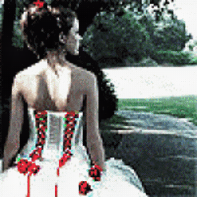 A Woman In A White Dress With Red Flowers On The Back Is Standing In Front Of A Lake GIF