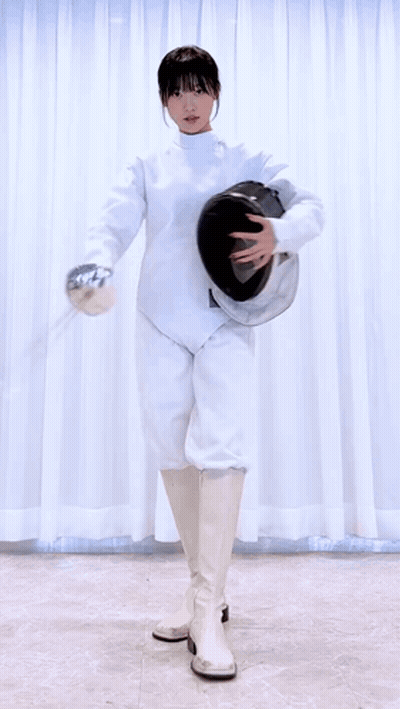 A Woman In A White Fencing Outfit Is Holding A Helmet And A Sword . GIF