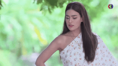 A Woman In A White Floral Dress Is Standing In Front Of A Tree . GIF