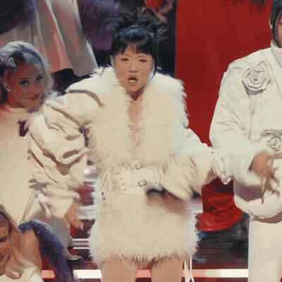 A Woman In A White Fur Coat Stands In Front Of A Red Background GIF