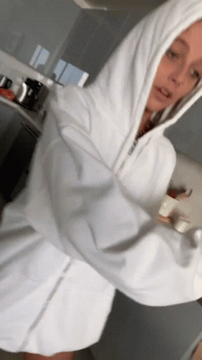 A Woman In A White Hoodie Is Standing In A Kitchen With Her Arms Outstretched . GIF