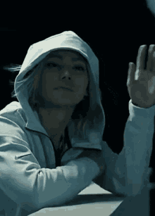 A Woman In A White Hoodie Is Waving Her Hand In The Dark GIF