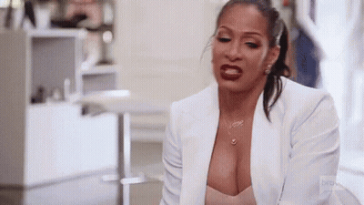 A Woman In A White Jacket And A Plunging Neckline Is Sitting On A Couch . GIF