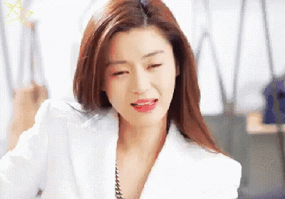 A Woman In A White Jacket And Red Lipstick Is Sitting In An Office . GIF