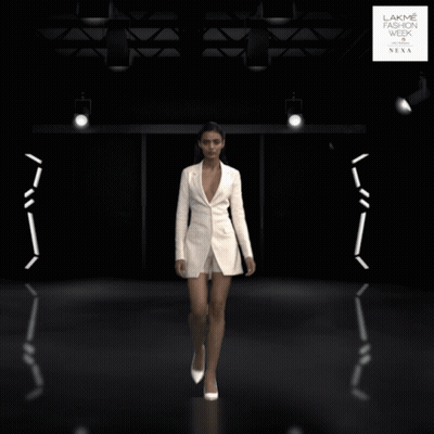 A Woman In A White Jacket And Shorts Is Walking Down A Runway At The Lakme Fashion Week GIF
