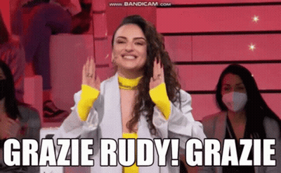 A Woman In A White Jacket And Yellow Top Is Smiling And Says Grazie Rudy Grazie GIF