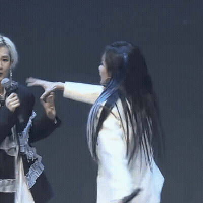 A Woman In A White Jacket Holds A Microphone While A Woman In A Black Shirt Holds A Microphone In Her Hand GIF